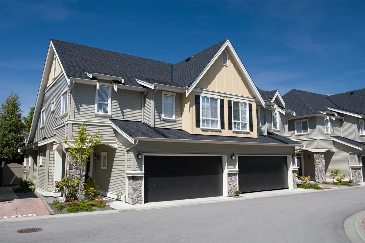 Attached two-story homes with gray lap siding, a board-and-batten gable and paired garage doors facing a private drive — duplex insurance in Connecticut
