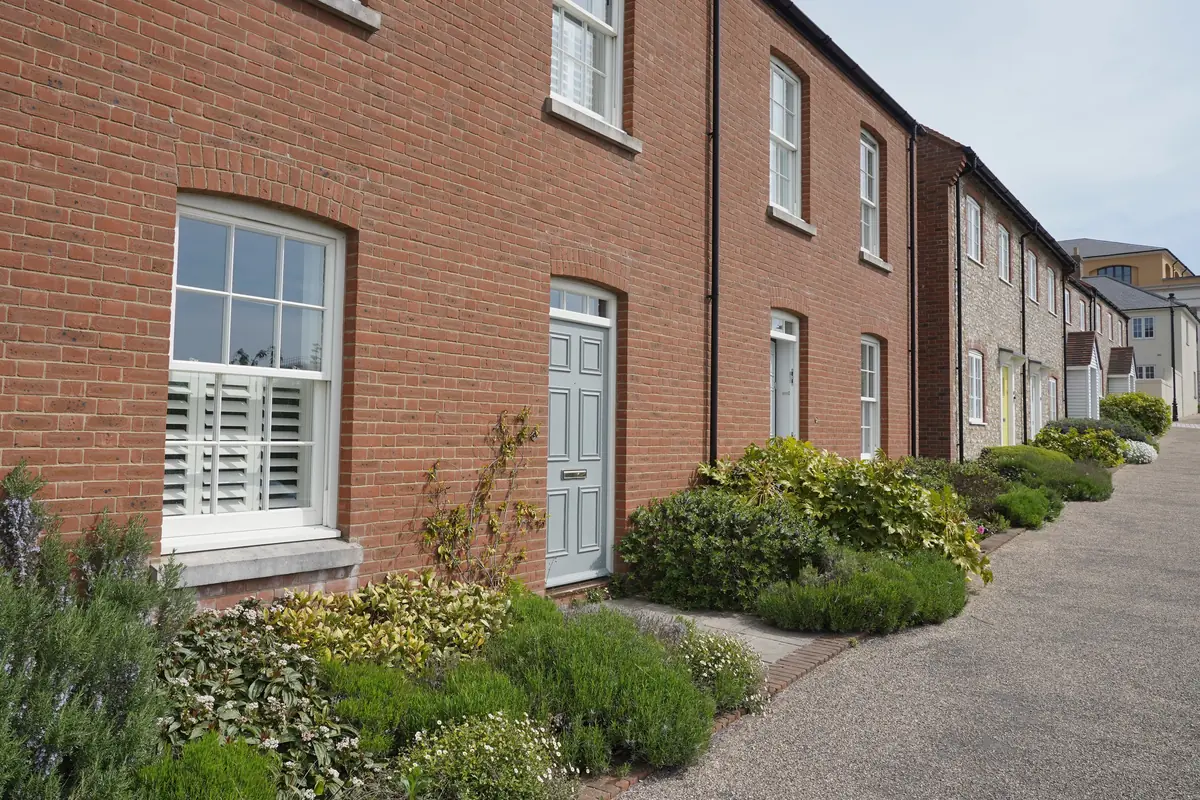 A terrace of attached brick houses with white sash windows and painted panelled front doors, along a planted path