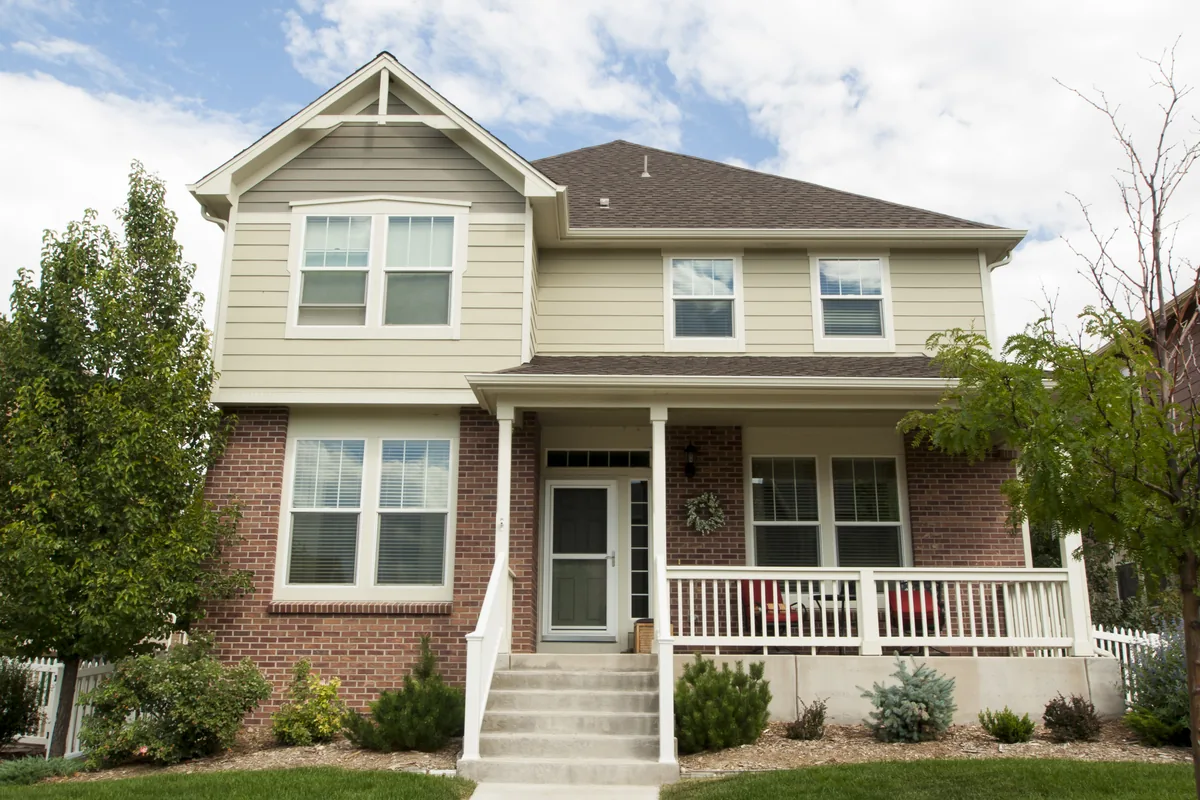 A two-story single-family rental house with cream lap siding above red brick, a covered front porch with white railing, and a concrete walkway across a mown lawn