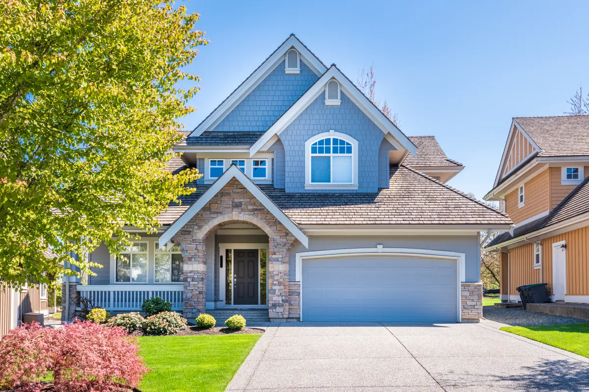 A two-story house with blue-gray shingle siding, a stone-faced arched entry and an attached two-car garage beside a concrete driveway