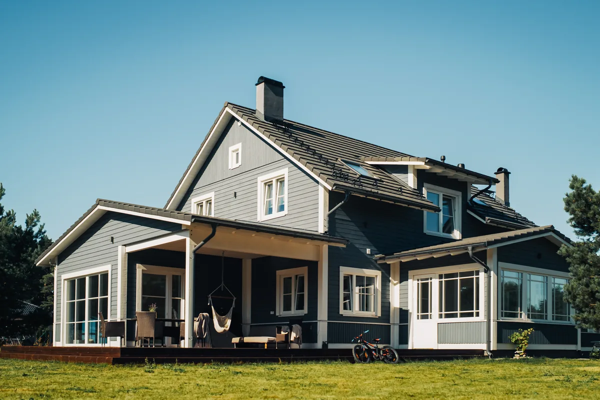 The garden elevation of a dark gray timber-clad house with white trim, a covered veranda with wicker seating, and a mown lawn