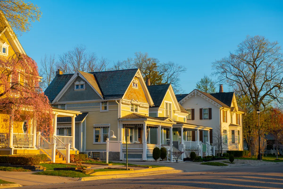 A street of older wood-frame houses with decorative gable trim and covered front porches, in evening light